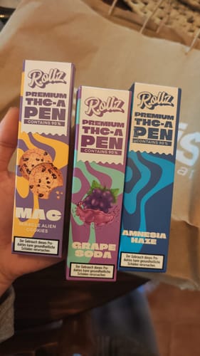 Customer holding the packaging for three ROLLZ THCA Vape pens in MAC, Grape Soda, and Amnesia Haze flavors.