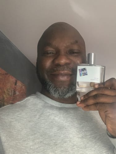 Reviewer smiling while holding the clear glass bottle of For Him Pheromone Perfume.