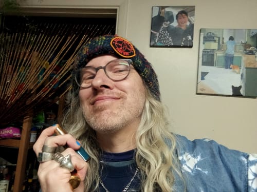 A happy reviewer smiles while holding the Honeyberry perfume bottle to their neck, enjoying the scent.