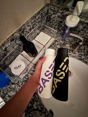 Reviewer holding the black and white Shower Duo bottles over a bathroom sink.
