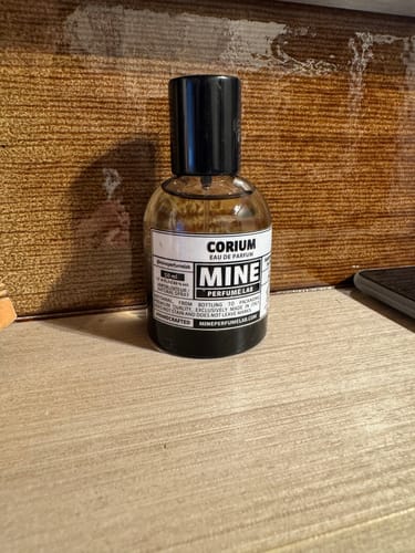 Recensione del cliente: il flacone del profumo CORIUM su una superficie in legno.