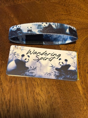 Customer's blue Wandering Spirit Bracelet with a panda print, shown next to its matching card on a wooden surface.