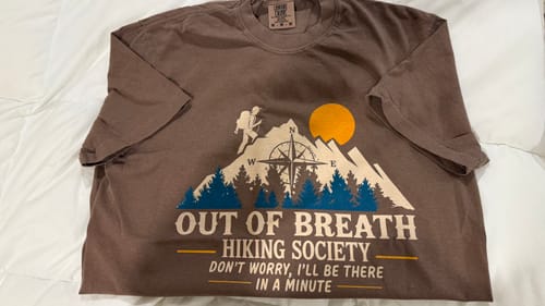 Customer's brown Out Of Breath T-shirt with a hiking graphic laid flat on a white surface.