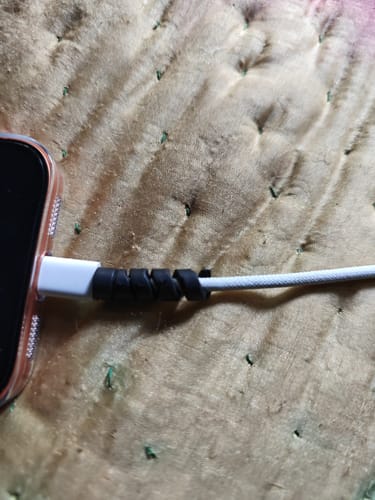 Close-up of a reviewer's black Cable Protector wrapped around a white charging cable plugged into a phone.