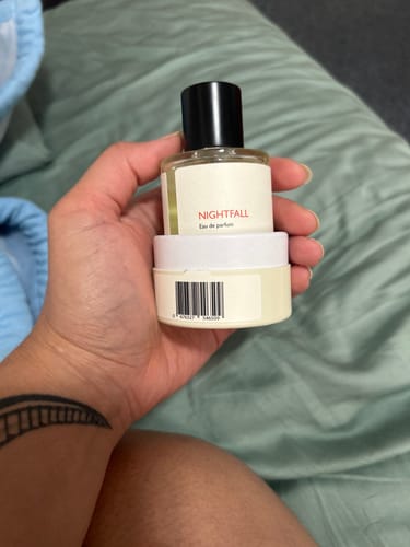 Customer holding a clear bottle of Nightfall perfume on top of its white packaging.