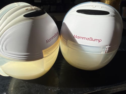 Customer's two Luna© Wearable Breast Pumps on a dark surface, both containing collected milk.