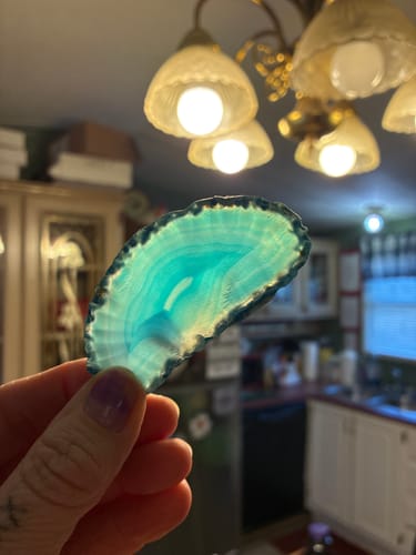 Customer holding a beautiful teal agate slice from their AuraBloom Subscription Box up to the light.