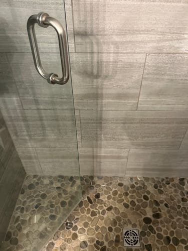 Customer photo of a clean shower with glass doors and a pebble floor after using the Ultimate Home Bundle.