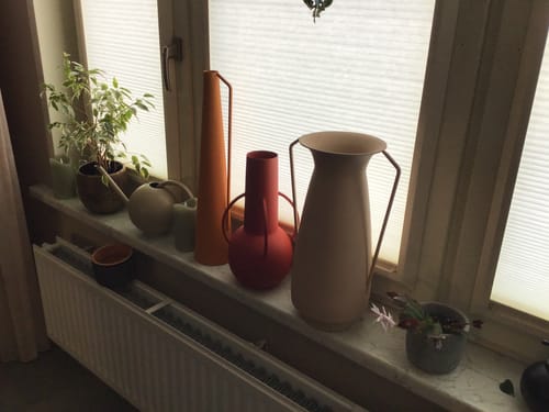 Recensent toont de kleurrijke POLSPOTTEN Roman Vaas Set op een vensterbank.