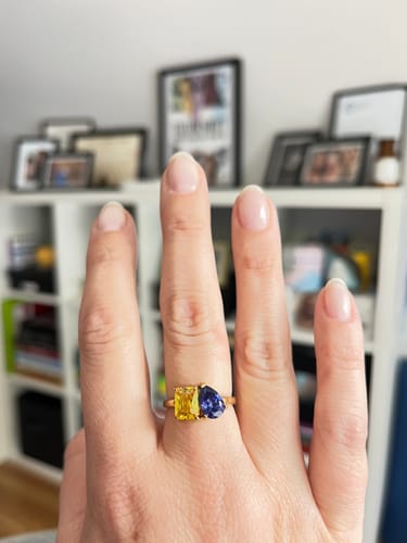 Customer's hand showing the Toi Et Moi Birthstone Ring with a yellow emerald-cut stone and a blue pear-cut stone.