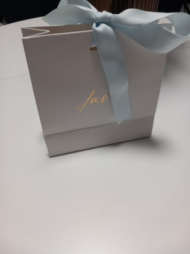 Kundenfoto der weißen Geschenktüte für die Geschenkbox, die mit einer blauen Schleife zugebunden ist.