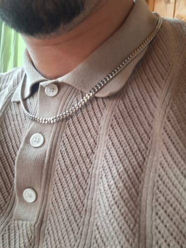 Primer plano de un cliente que lleva la Cadena Miami Cuban de 5 mm sobre el cuello de una camisa tipo polo beige.