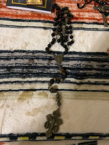 Customer's vintage-style rosary with black obsidian beads and a Pardon Crucifix laid out on a striped blanket.
