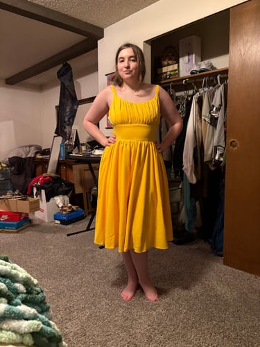 Reviewer showing the fit of the bright yellow Ingenue Dress while standing in a bedroom.