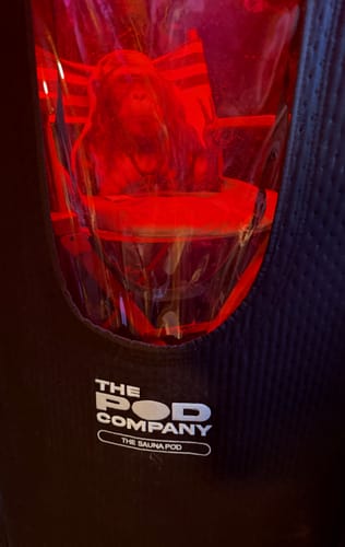 Close-up of The Sauna Pod, showing the logo with a person visible inside under red light.