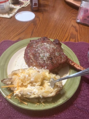 Customer's large cooked Tomahawk Ribeye served on a plate with a baked potato.