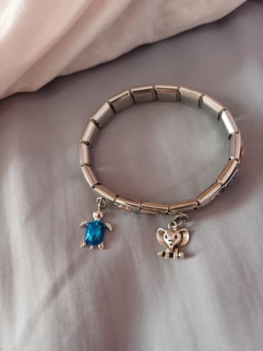 Una clienta muestra su pulsera italiana con el Charm Colgante Elefante plateado y un colgante de tortuga azul.