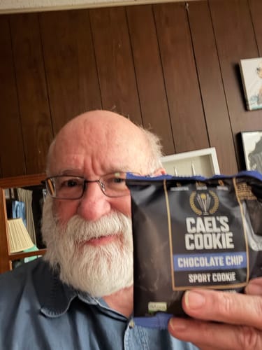 A reviewer smiles while holding up the packaging for a Cael's Cookie Chocolate Chip.