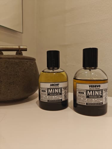 Recensore mostra la sua boccetta di profumo ARCHÉ su un ripiano accanto al profumo Vesevo.