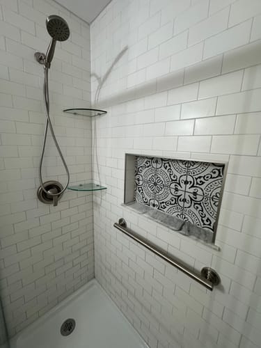 Customer's brushed nickel handheld shower head installed in a modern white subway tile shower stall.
