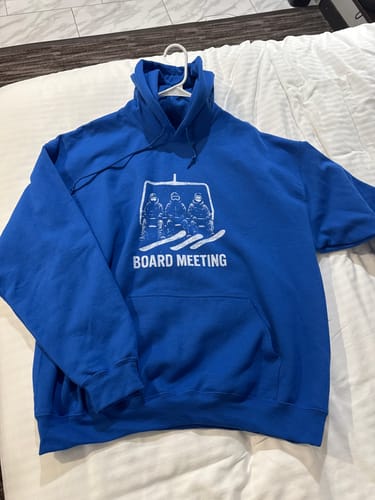 Customer's blue "Board Meeting" hoodie, featuring the snowboarder graphic, laid out on a bed.