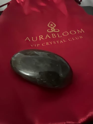 Customer's smooth, dark Monthly Crystal resting on the red VIP Crystal Club pouch.
