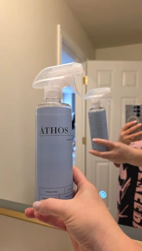 Customer holding the Áthos Glass & Window Concentrate bottle in front of a clean bathroom mirror.