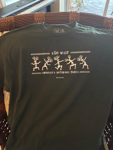 Reviewer's dark green Stay Wild Petroglyphs Tee with a white graphic laid out over a wicker chair.