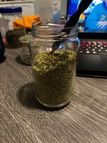 Customer's glass jar filled with green Exotic Shake on a desk, with a black tool inside.