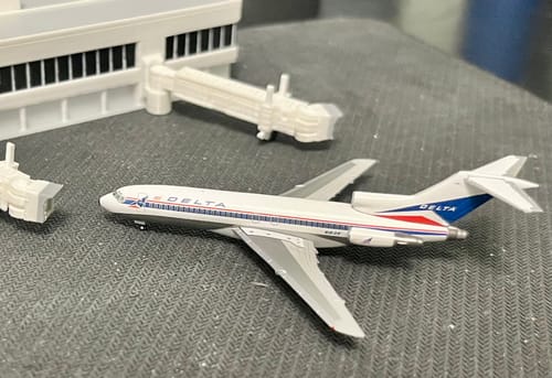Reviewer's HERPA DELTA 727-100 model with retro livery displayed near a model airport terminal.