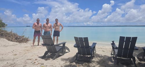 Reviewer on the left in Black Leaf Magenta Swim Trunks standing on a sunny beach with two friends.
