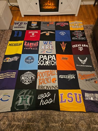 Reviewer's colorful Premium T Shirt Quilt made from various team shirts, spread out on a living room floor.