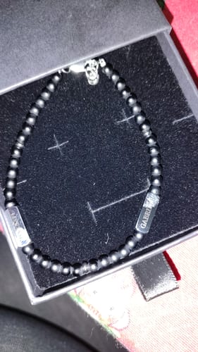 Customer's black beaded Tribute bracelet with engraved pendants and a skull charm, displayed in its gift box.