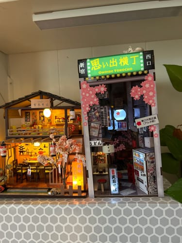 Customer's completed Omoide Yokocho Book Nook Kit, lit up on a shelf next to another miniature model.