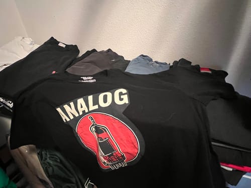 Customer's black Analog T-Shirt laid out on a pile of other shirts, showing the front graphic.