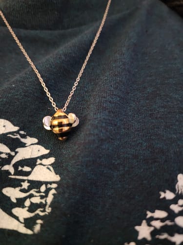 Customer's cute Adopt a Bee Necklace with its striped bee pendant shown against a dark patterned shirt.