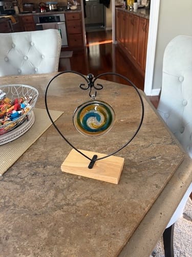 Reviewer's Glass Suncatcher with blue and yellow swirls, hanging in a black heart-shaped stand on a tabletop.