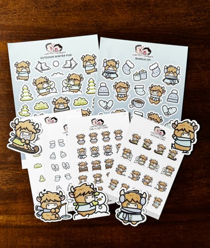 Customer's complete Winter Highland Cows Sticker Set, showing sticker sheets and die-cut cows on a dark wooden surface.