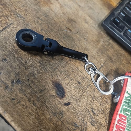 Reviewer's black 10mm Wrench Keychain attached to a key ring, resting on a wooden surface next to a keyboard.