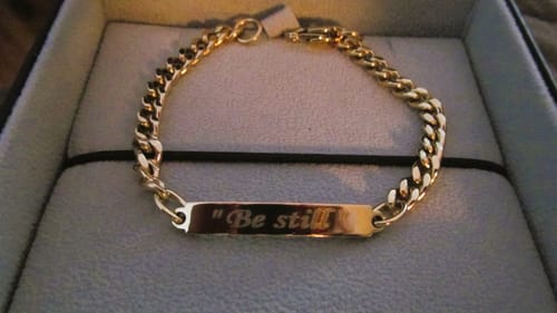 Reviewer's shiny gold Cuban Link ID Bracelet engraved with "Be still," shown in a jewelry box.