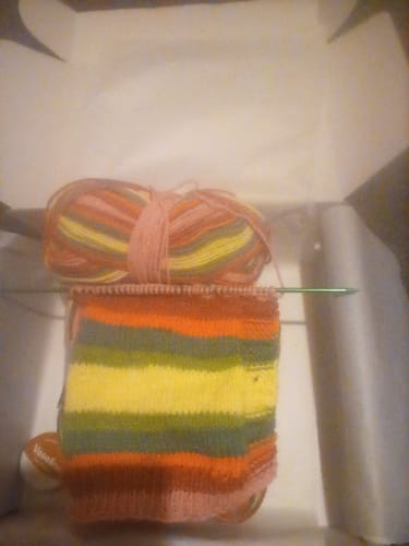 A customer's colorful striped knitting project in progress from the New Beginnings kit, with the ball of yarn visible.