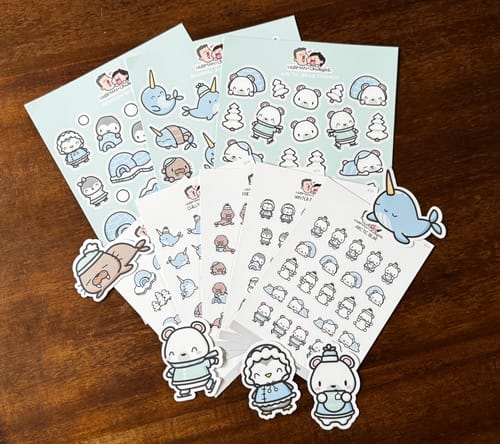 Customer's Arctic Winter Sticker Set spread on a table, showing cute character sheets and several larger die-cut stickers.
