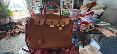 Customer's brown, structured LALUVA Warkin Bag with gold hardware resting on their lap indoors.