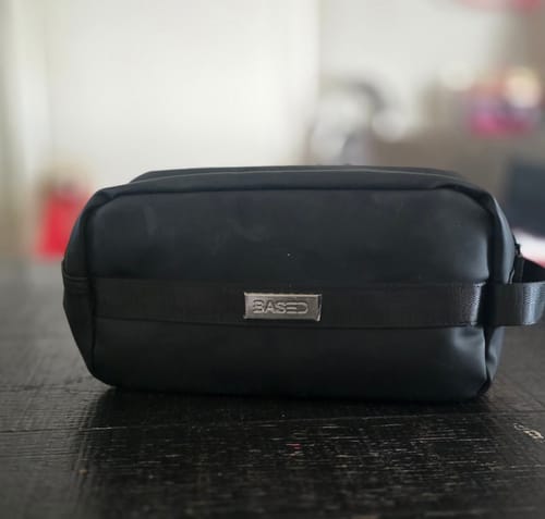 Customer's black Toiletry Bag with a silver logo plate, sitting on a dark wood table.