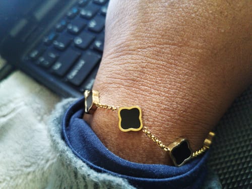 Close-up of a customer's wrist wearing a gold-colored bracelet with black clover-shaped charms.