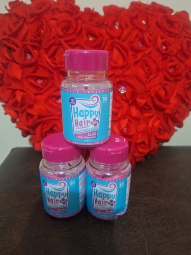 Cliente mostra os três potes de Happy Hair empilhados em frente a um coração vermelho decorativo.