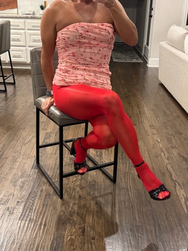 Reviewer sitting on a stool, wearing the shiny red Play Seamless Tights with a pink top.