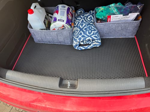 Recenzent pokazuje czarną matę do bagażnika z czerwoną obwódką, umieszczoną w bagażniku samochodu.