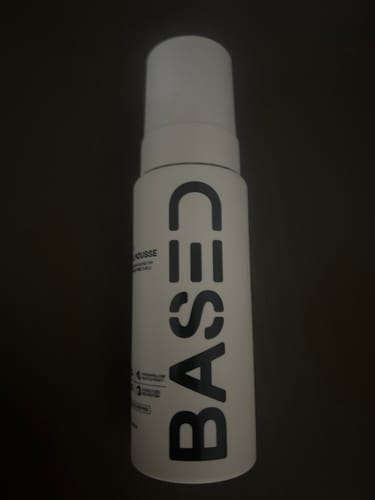 Customer's white bottle of Curl Mousse with prominent black lettering, shown on a dark surface.