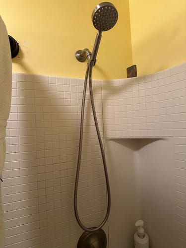 Customer's handheld shower head set installed in a tiled shower, showing the long, flexible metal hose.